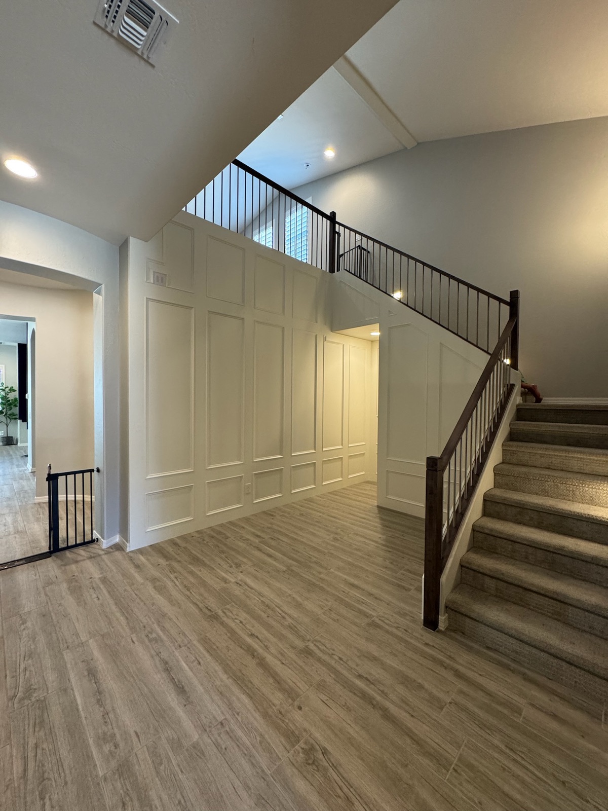 Two-story entryway before-and-after: bare walls transformed with full-height white wainscoting panels along the staircase